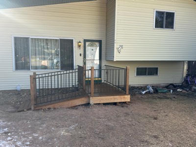 New entry deck with access ramp and black metal railings on a tan sided home