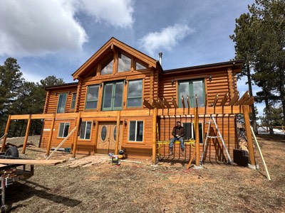 Cedar pergola framing across the front of a log home under a blue sky
