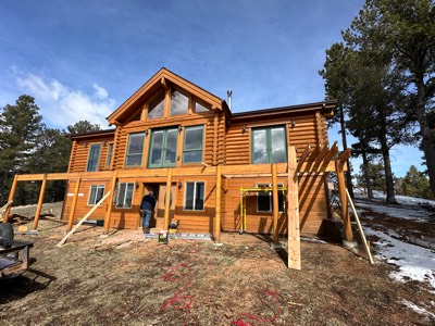 Pergola posts and beams being framed on a log home with snow on the ground